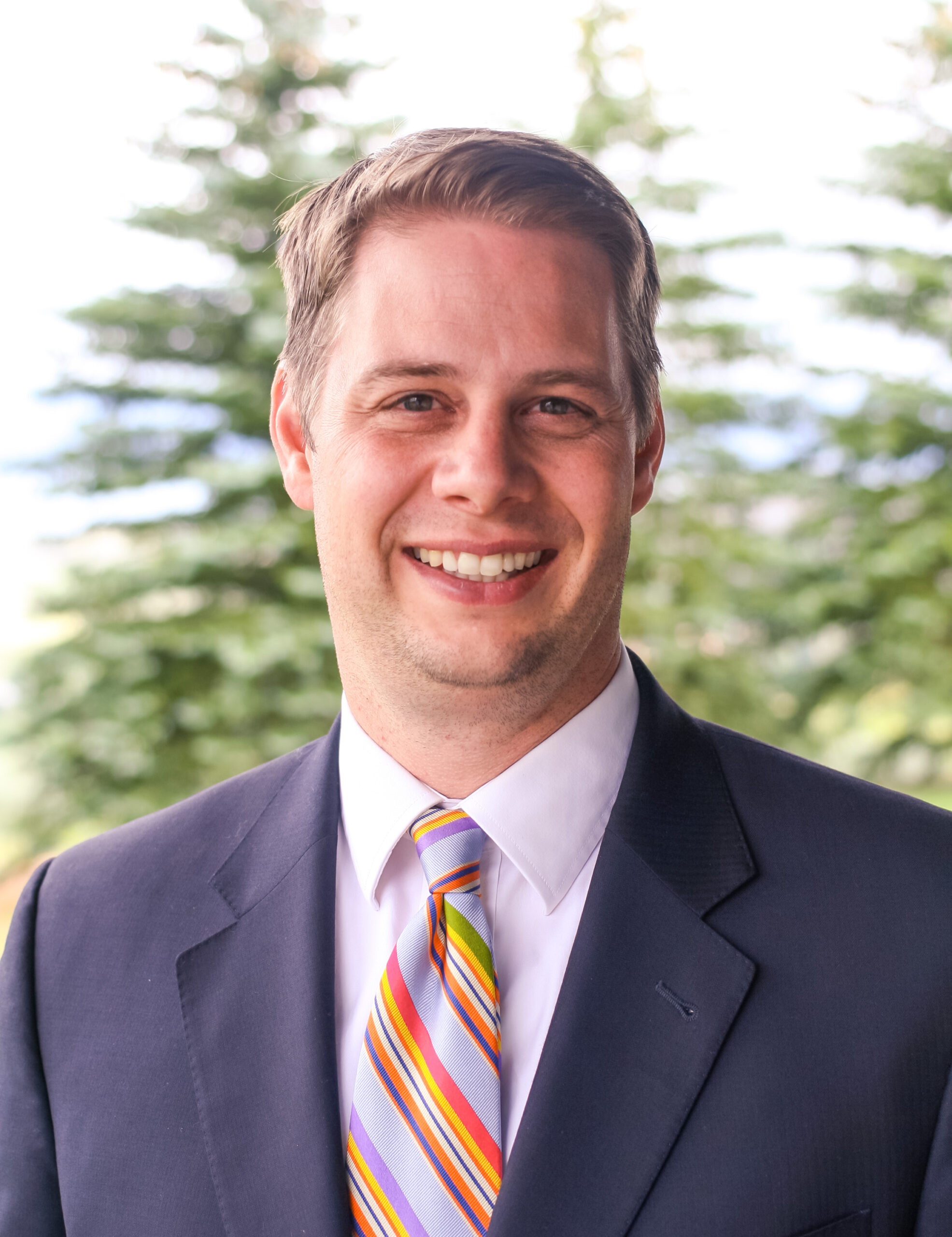 Professional headshot of attorney Jeffrey Q. Cardon wearing a navy suit and striped tie outdoors with trees in the background.