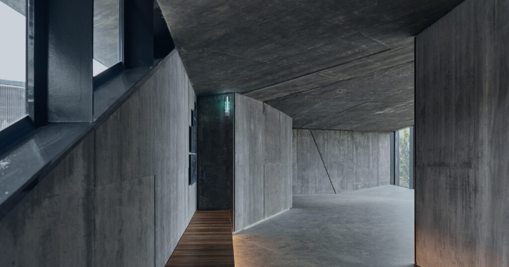 Modern concrete interior with layered walls, a wooden walkway, and an open passage ahead.